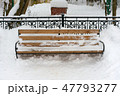 a snowy wooden bench and metal hedge behind  47793277