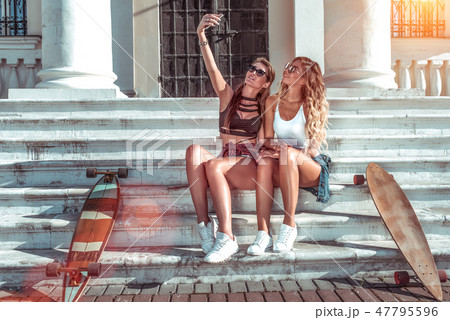 Beautiful girls girlfriends in summer city. Sit on steps next to longboard skateboard. Photographs Beautiful girls girlfriends in summer city. Sit on steps next to longboard skateboard. Photographs 47795596