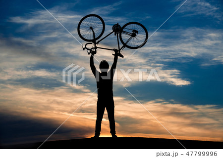 Man lifting bicycle at sunset sky. Man lifting bicycle at sunset sky. 47799996