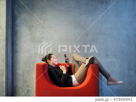 A young businesswoman with smartphone sitting on red armchair in office. A young businesswoman with smartphone sitting on red armchair in office. 47800941