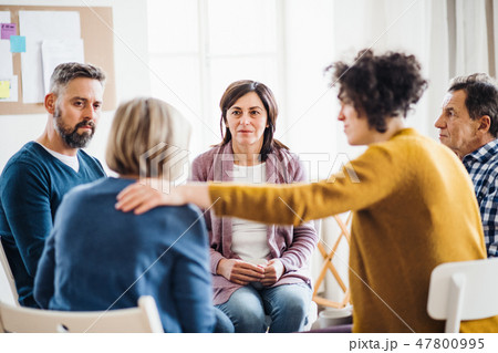 Men and women sitting in a circle during group therapy, supporting each other. 47800995