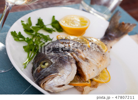 Top view of whole grilled dorada served with lemon and greens at plate 47807211