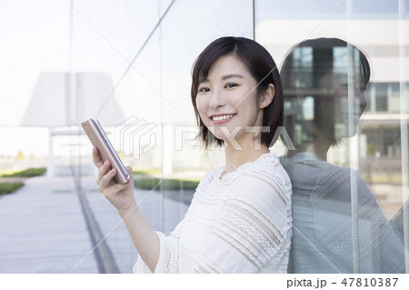 ガラスの壁に寄り掛かってスマホを操作する女子大生 ガラスの壁に寄り掛かってスマホを操作する女子大生 47810387