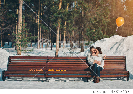 Valentine's day: a couple in love sitting on a bench in a winter forest with an orange balloon and Valentine's day: a couple in love sitting on a bench in a winter forest with an orange balloon and 47817153