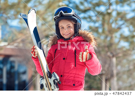 Winter vacation. Girl in goggles and helmet with skis standing outdoors smiling happy showing thumb 47842437