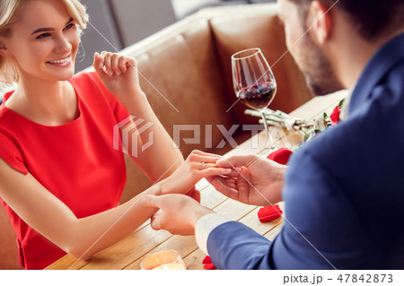Young couple on date in restaurant sitting man holding hand of woman wearing proposal ring cheerful 47842873