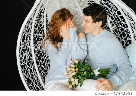 Couple girl and guy hugging on a big chair with a bouquet of roses. Couple girl and guy hugging on a big chair with a bouquet of roses. 47842953