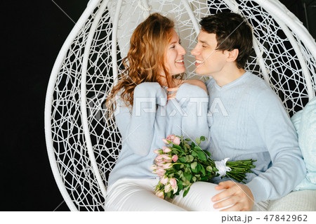 Couple girl and guy hugging on a big chair with a bouquet of roses. Couple girl and guy hugging on a big chair with a bouquet of roses. 47842962