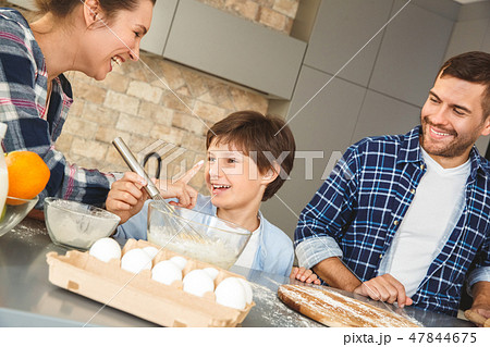Family at home standing at table in kitchen together mother touching son with hands dirty in flour Family at home standing at table in kitchen together mother touching son with hands dirty in flour 47844675