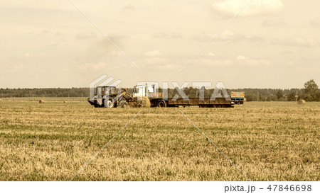 Farmer on a tractor picks haystack and loads bale of hay into the trailer, agriculture Farmer on a tractor picks haystack and loads bale of hay into the trailer, agriculture 47846698