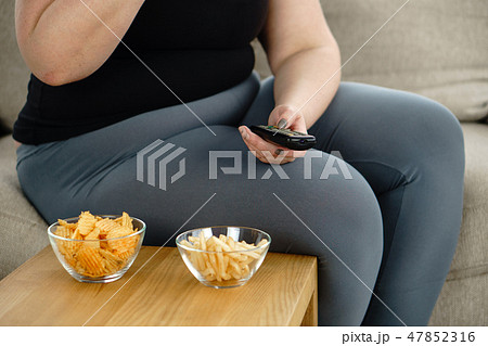 fat woman watching series at tv eating junk food 47852316