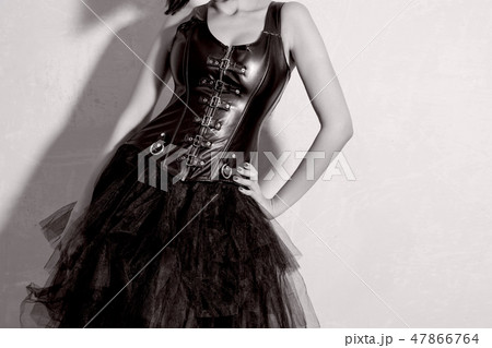 Busty girl in leather corset. Young dominant woman stands near the wall. 47866764