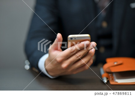 スマートフォン(スマホ)を持つスーツのビジネスマンの手。ビジネスシーン。 スマートフォン(スマホ)を持つスーツのビジネスマンの手。ビジネスシーン。 47869811