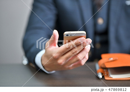 スマートフォン(スマホ)を持つスーツのビジネスマンの手。ビジネスシーン。 スマートフォン(スマホ)を持つスーツのビジネスマンの手。ビジネスシーン。 47869812