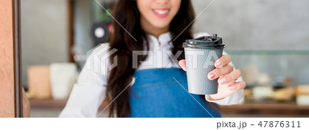 Young female cafe staff giving takeaway coffee cup Young female cafe staff giving takeaway coffee cup 47876311