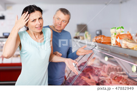 Sad couple customers choosing meat in shop Sad couple customers choosing meat in shop 47882949
