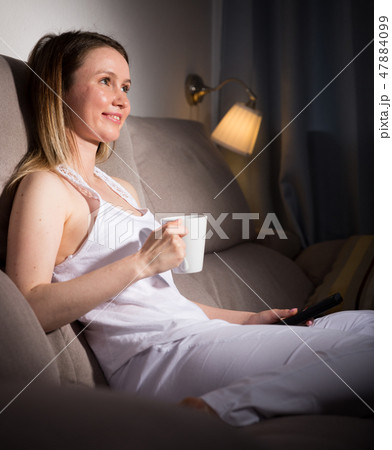Young woman is sitting in plaid with tea and watching TV 47884099