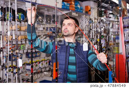 calm male choosing fishing rod for fishing in the sports shop calm male choosing fishing rod for fishing in the sports shop 47884549