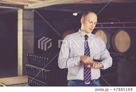 Confident male winemaker degusting red wine in wine cellar near bottles racks Confident male winemaker degusting red wine in wine cellar near bottles racks 47885169