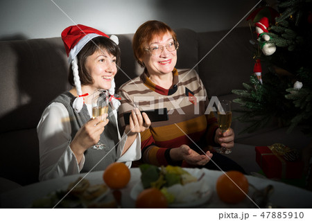 Happy mother and daughter drink champagne and watch TV on Christmas night Happy mother and daughter drink champagne and watch TV on Christmas night 47885910