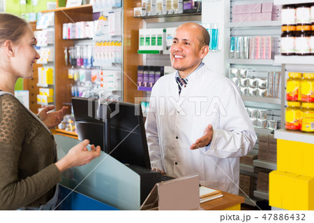 Pharmacist serving client in pharmacy . Pharmacist serving client in pharmacy . 47886432