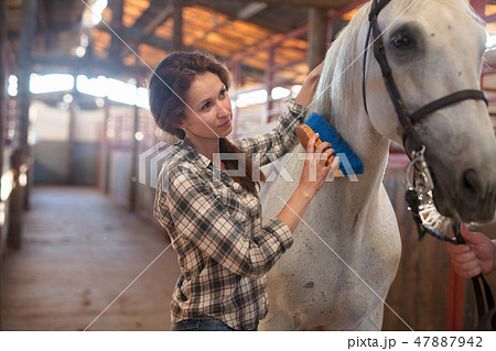 Woman farmer standing with white horse at stabling indoor 47887942