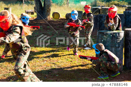 Children paintball players of opposite teams playing in shootout outdoors Children paintball players of opposite teams playing in shootout outdoors 47888146