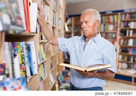 Senior male interested in books looking for necessary literature on shelves 47888697