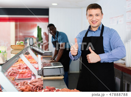 Proud male owner of butcher shop standing behind counter, giving thumbs up 47888788