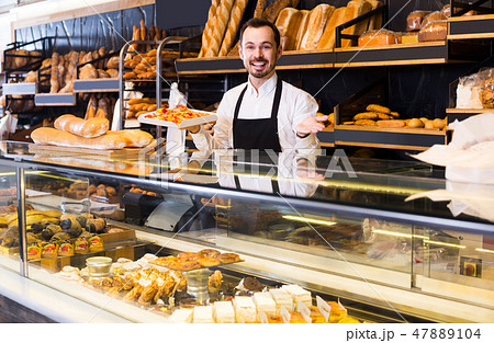 Male shop assistant demonstrating fresh delicious pastry in bakery Male shop assistant demonstrating fresh delicious pastry in bakery 47889104