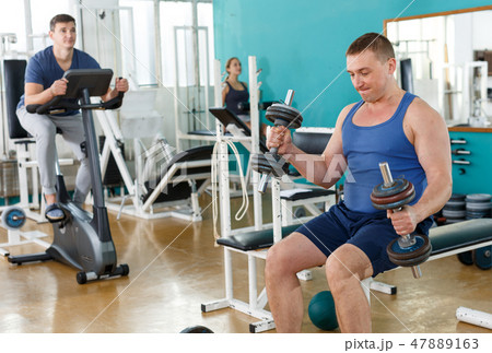 Positive man doing exercises with dumbbells Positive man doing exercises with dumbbells 47889163