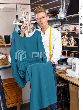 Tailor holding dress at his workplace Tailor holding dress at his workplace 47889659