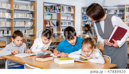 Group of school kids studying in school library with friendly female teacher 47889920