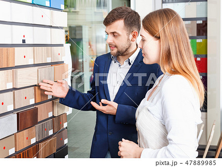 Competent seller in showroom helping young female client to choose furniture materials for her apartment Competent seller in showroom helping young female client to choose furniture materials for her apartment 47889985