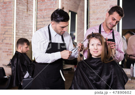 Two hairdressers making hairstyle for female client 47890602