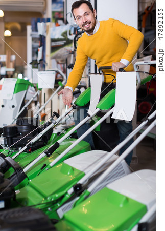 interested guy deciding on best lawnmower in garden equipment shop interested guy deciding on best lawnmower in garden equipment shop 47892155