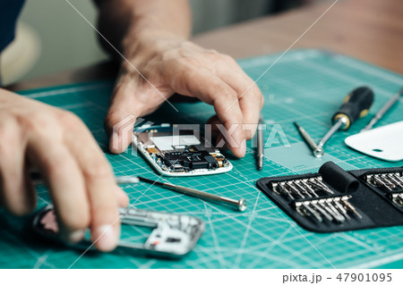 Electronics repair service. Technician disassembling smartphone for inspecting 47901095