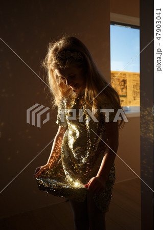 A seven-year-old girl dressed in a smart dress decorated with gold sparkles is standing in the room A seven-year-old girl dressed in a smart dress decorated with gold sparkles is standing in the room 47903041
