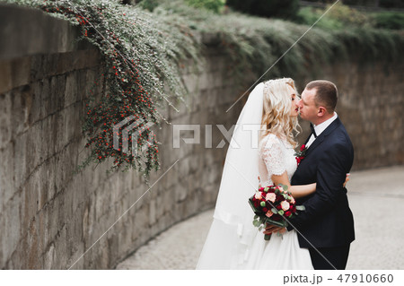 Stylish couple of happy newlyweds walking in the park on their wedding day with bouquet Stylish couple of happy newlyweds walking in the park on their wedding day with bouquet 47910660
