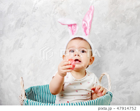 Portrait of a cute baby dressed in Easter bunny ears in a basket holds egg happy easter concept 47914752