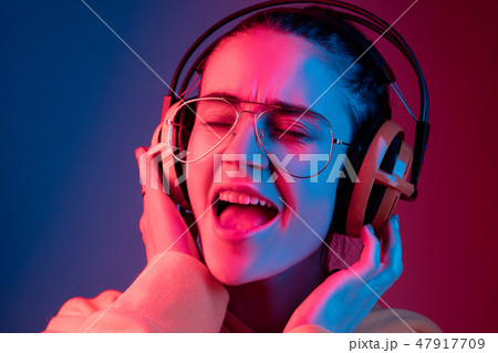 Fashion pretty woman with headphones listening to music over neon background Fashion pretty woman with headphones listening to music over neon background 47917709