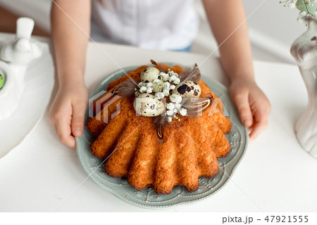 Little girl's hands hold a plate with easter cupcake decorated with easter eggs and feathers 47921555
