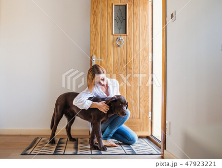 A young woman sitting indoors by the door on the floor at home, playing with a dog. A young woman sitting indoors by the door on the floor at home, playing with a dog. 47923221