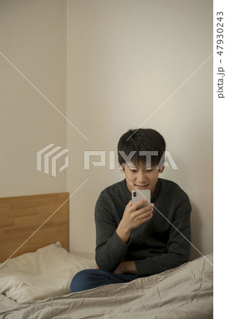 ベッドでスマートフォンを使う男の子 寝不足 中学生 高校生 ベッドでスマートフォンを使う男の子 寝不足 中学生 高校生 47930243