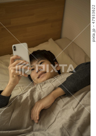 ベッドでスマートフォンを使う男の子 寝不足 中学生 高校生 ベッドでスマートフォンを使う男の子 寝不足 中学生 高校生 47933622
