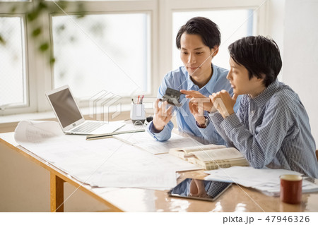 信頼のおける先輩から一級建築士の試験勉強を教えてもらい嬉しそうに楽しく勉強する若い男性会社員 47946326