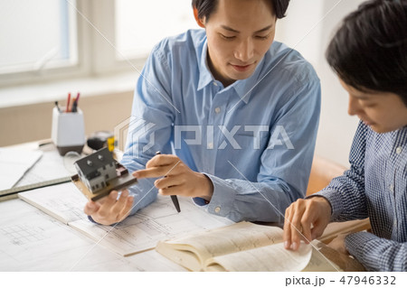 笑顔優しい先輩から一級建築士の試験勉強を教えてもらい嬉しそうに楽しく勉強する若い男性会社員 47946332
