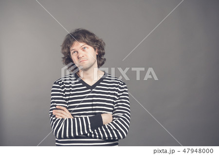 Studio shot of pensive young European male with voluminous hair posing at blank wall, keeping arms 47948000