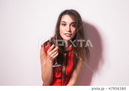 Party, holidays and celebrations concept - Cheerful charming young woman in red dress drinking 47956380