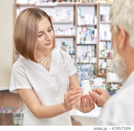Pretty pharmacist helping old man with pills. Pretty pharmacist helping old man with pills. 47957509